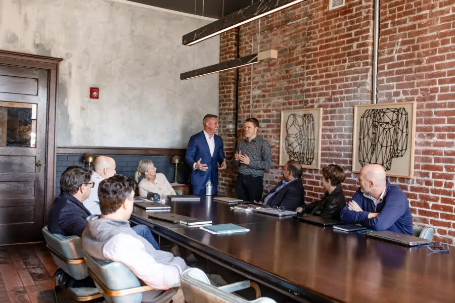 A group of professionals sitting in a brick room at a large table discussing business plans.