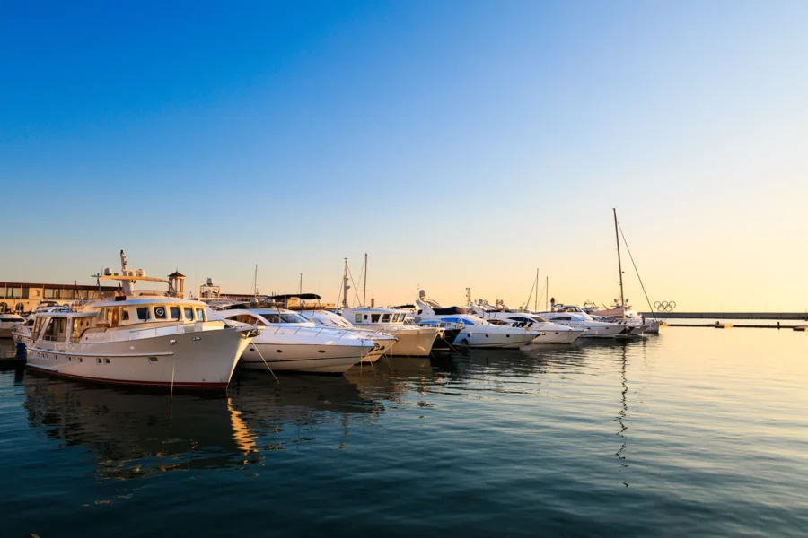 Several yachts and boats are docked at a marina during sunset, with calm water reflecting the clear sky.